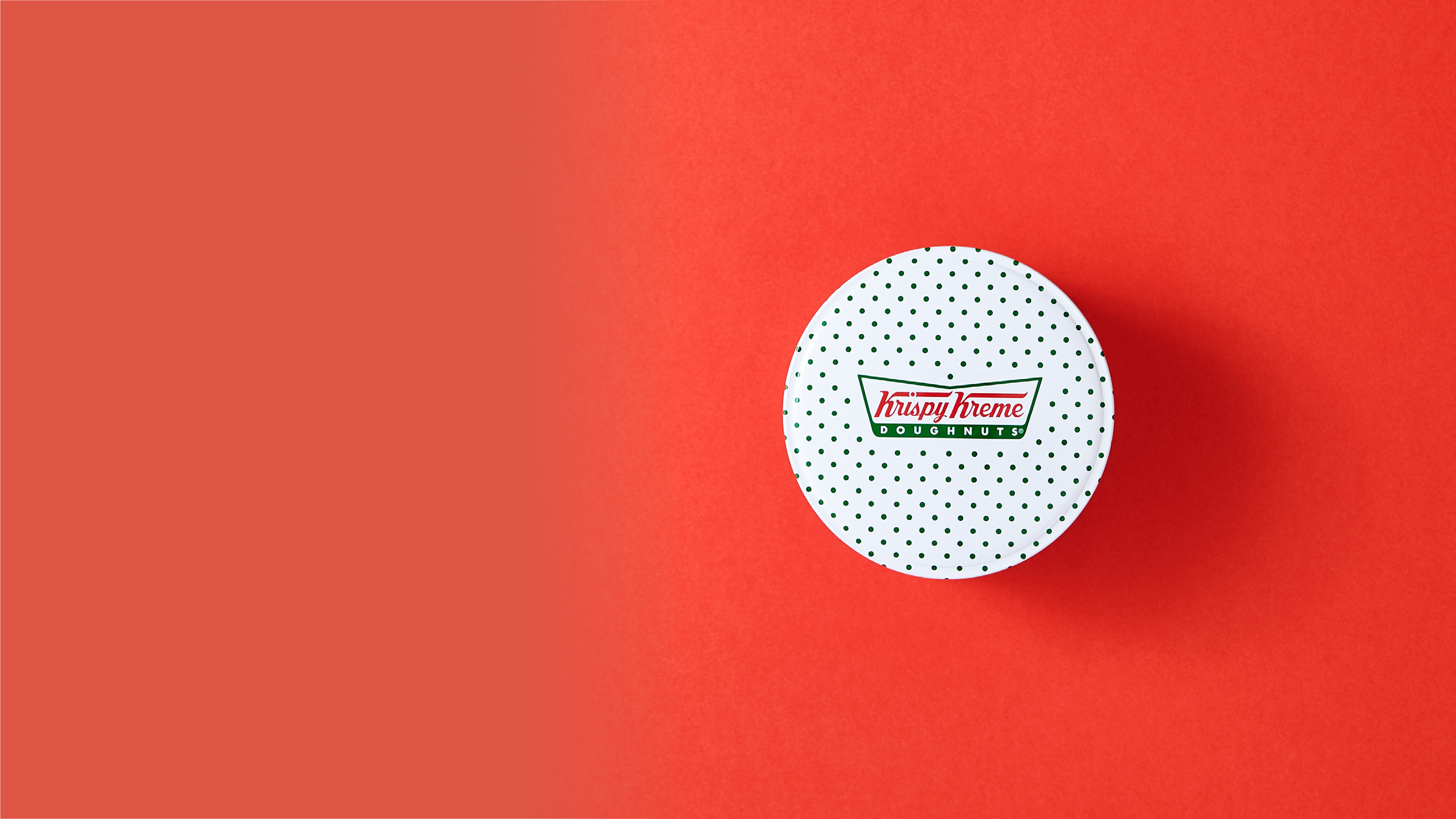 Een verpakking van een Krispy Kreme-donutblik tegen een rode achtergrond.